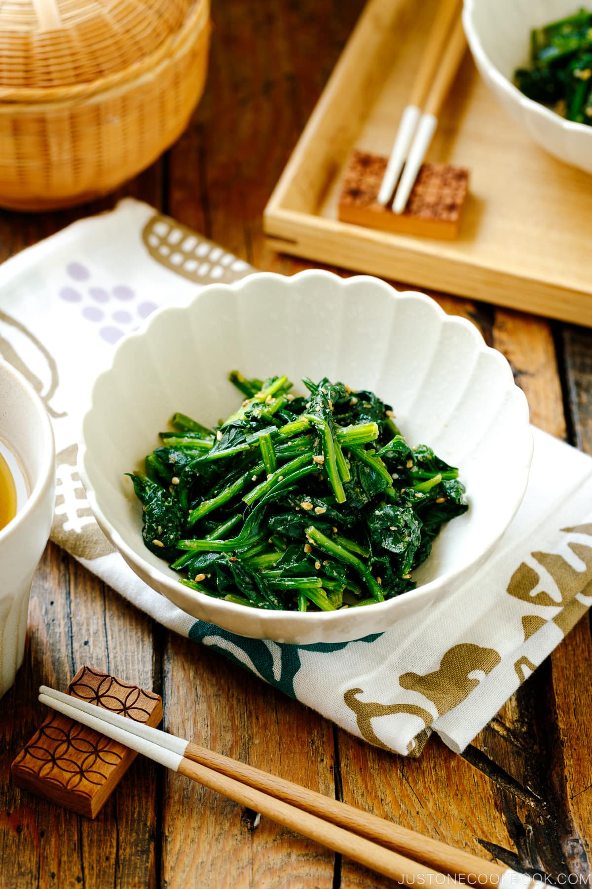 A white fluted dish containing Japanese spinach salad seasoned with sesame seeds, soy sauce, and sugar.