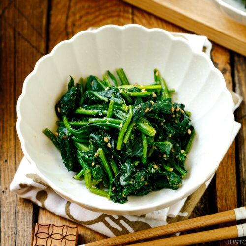A white fluted dish containing Japanese spinach salad seasoned with sesame seeds, soy sauce, and sugar.